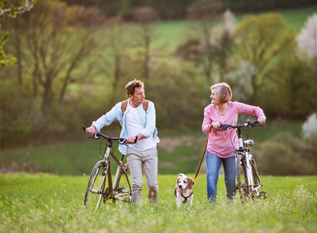 Beautiful senior couple with bicycles and dog outside in spring nature.